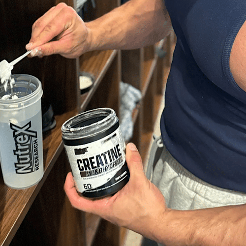 Persona preparando un batido con Nutrex Creatine Drive en un vaso con agua.